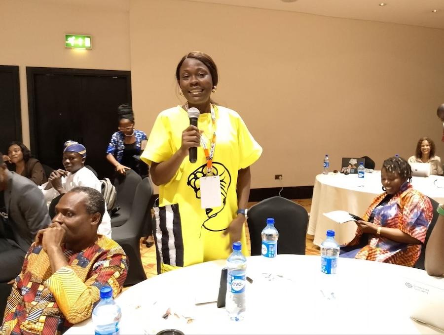 a woman in yellow holds a microphone and speaks at an event room