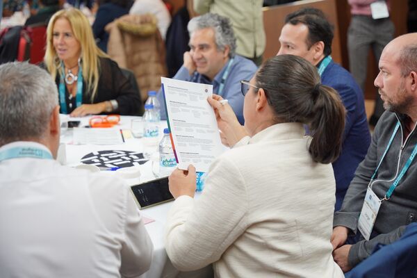 A group of people seated at a table, reviewing documents and discussing ideas together.