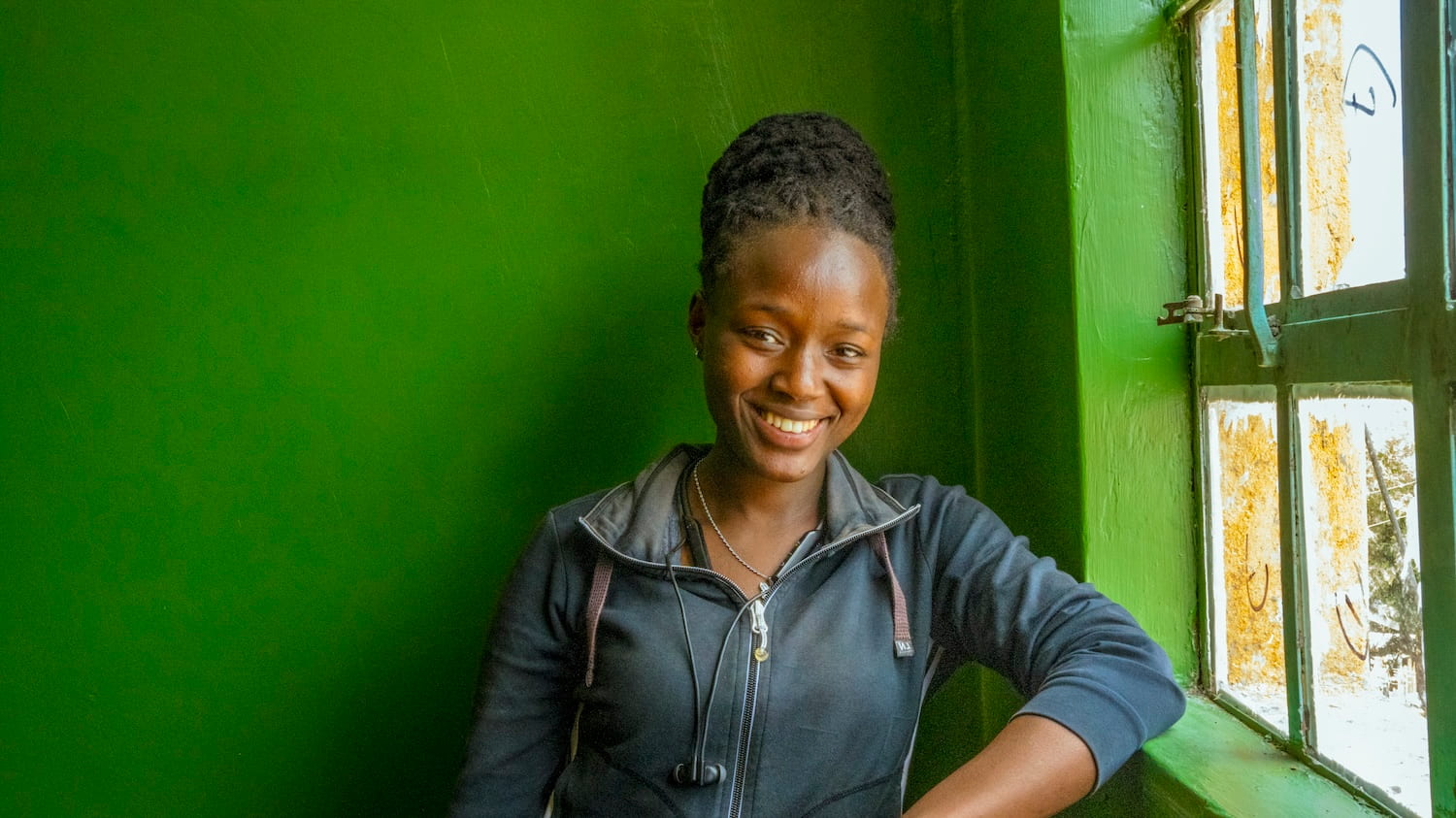 A smiling woman stands confidently in front of a vibrant green wall